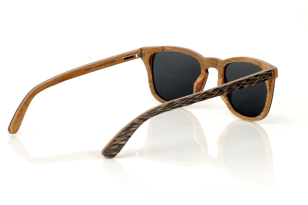 Wood eyewear of Jichimu RISKY. RISKY wooden sunglasses combine a classic shape that flatters all face types with a more contained size, creating a versatile and always on-trend accessory. They are meticulously manufactured using a three-strip laminate technique: black Chicken Wing wood on the outside, maple in the center that provides luminosity, and oak on the inside, offering exceptional resistance. The temples replicate this tricolor pattern, guaranteeing coherence and style throughout the entire set. What really makes the RISKY stand out is the unique texture of its front, accented with eye-catching oak rivets. Measuring 140x47mm and a caliber of 49, these glasses are the perfect balance between comfort and style statement. for Wholesale & Retail | Root Sunglasses® 